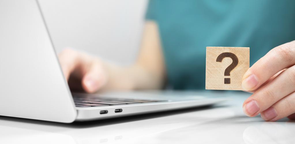 Frau sitzt am Laptop und hat einen block mit Fragezeichen in der Hand
