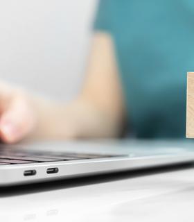 Frau sitzt am Laptop und hat einen block mit Fragezeichen in der Hand